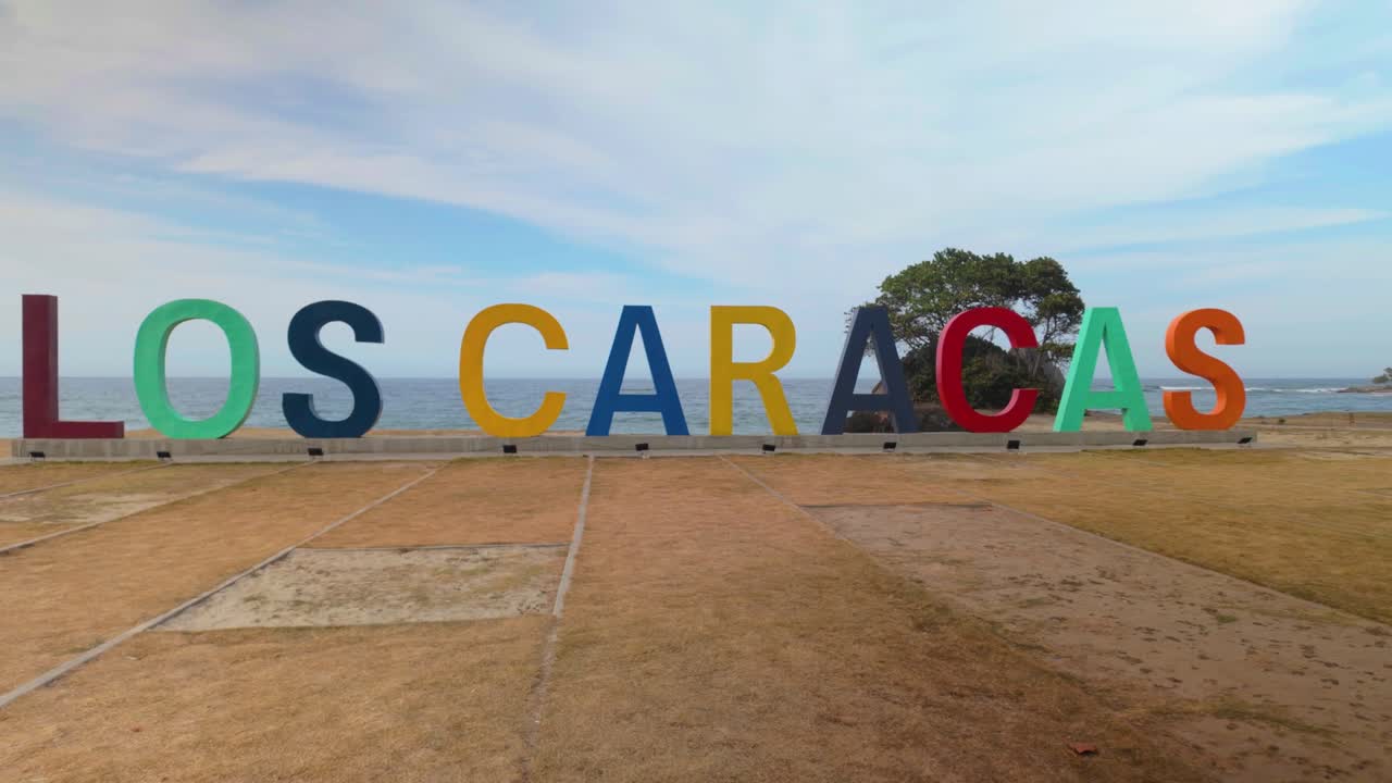 Colorful landmark sign for "Los Caracas" at a beachside location, overlooking the ocean