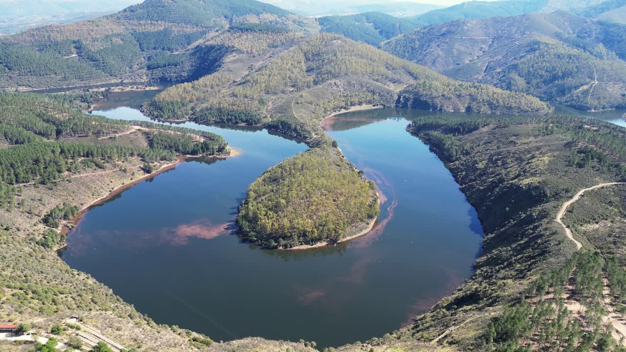 Un fiume serpeggiante che circonda un'isola lussureggiante e verde in mezzo a un terreno collinare. Ideale per documentari ambientali o contenuti di viaggio