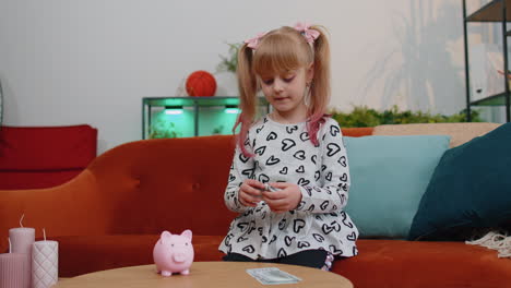 niña pequeña poniendo billetes de dólar para futuras compras de regalos en la alcancía en casa