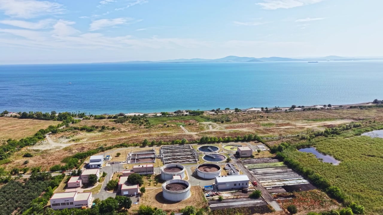 Coastal wastewater treatment facility near a large body of water with clear sky and distant mountains