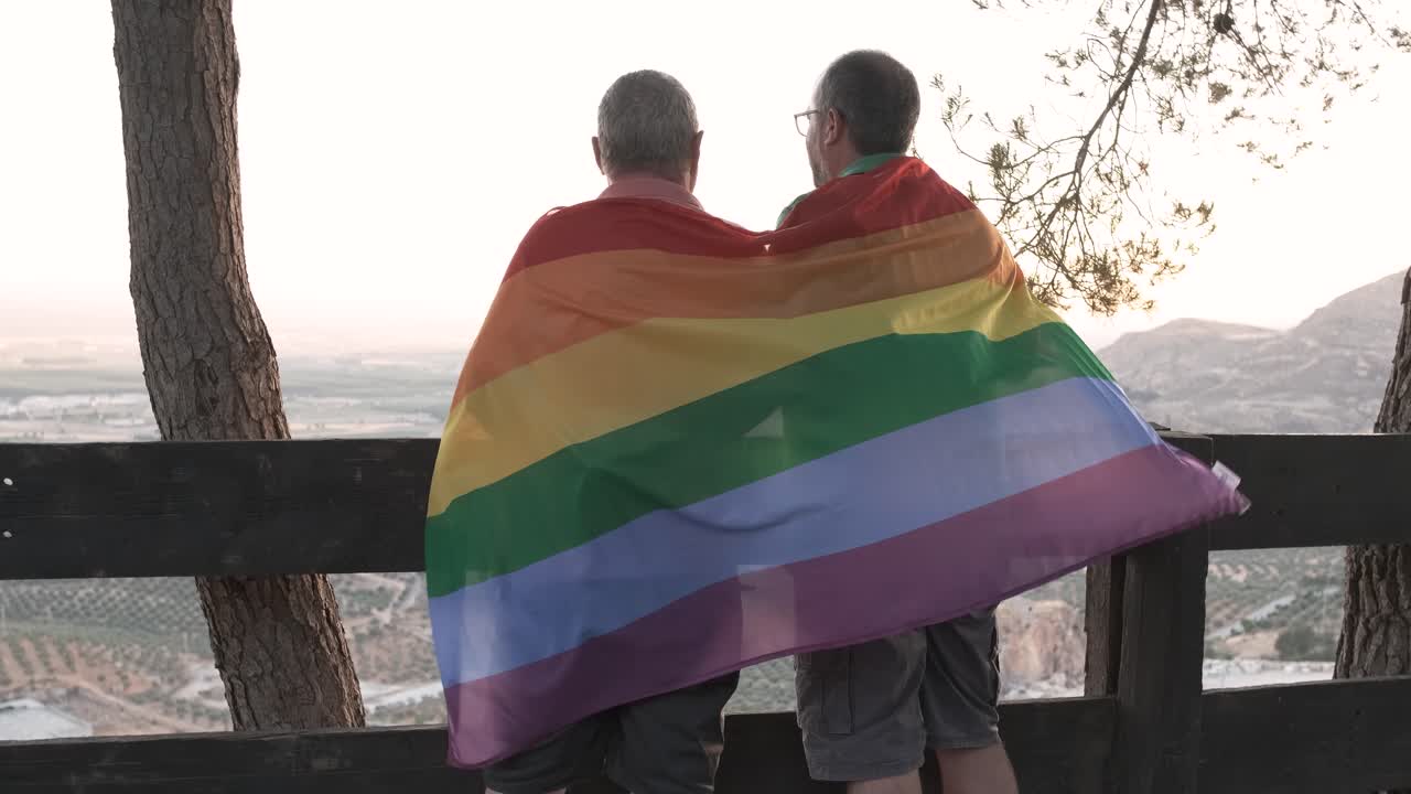 Two men with pride flag enjoying the sunset view