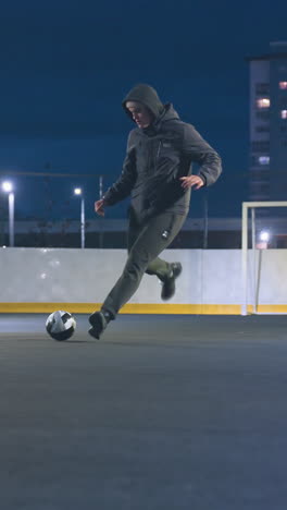 player kicks soccer ball toward goal post during intense urban night practice, ball rolls out after hitting goal, surrounded by illuminated city buildings