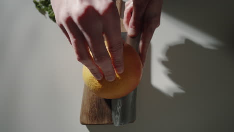 hands cutting grapefruit in half in the kitchen at home on wooden cutting board with sharp knife