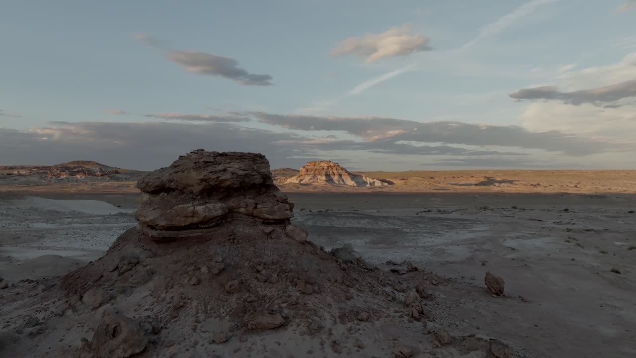vuelo por una colina del desierto para revelar otra formación colorida iluminada por la puesta de sol