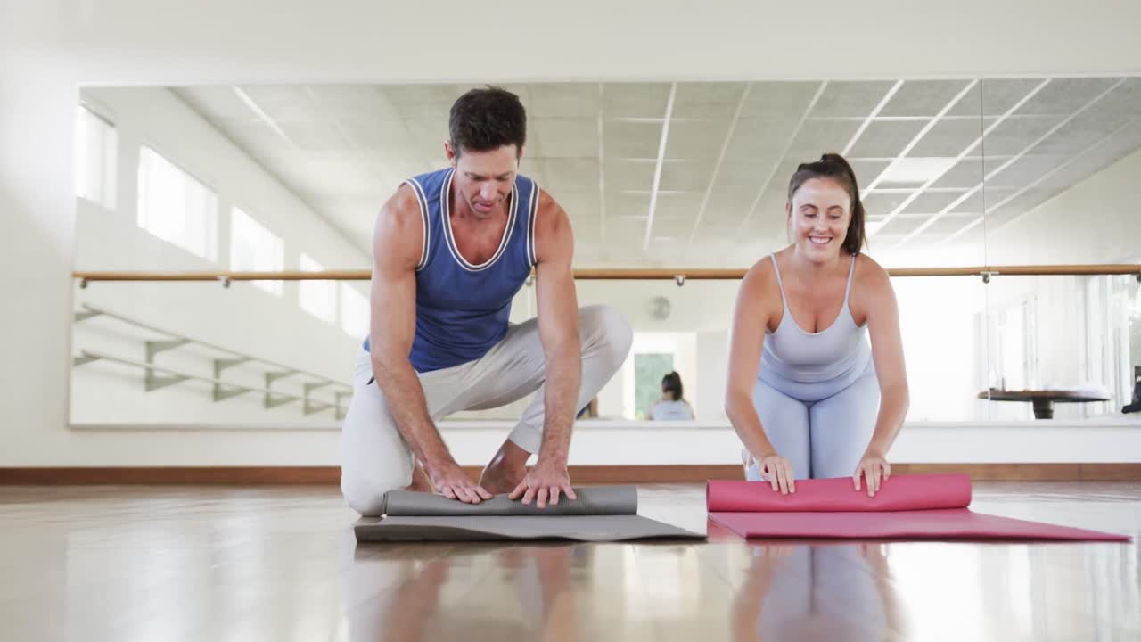 hombre caucásico feliz y instructora de yoga enrollando esteras después de practicar en el gimnasio, cámara lenta