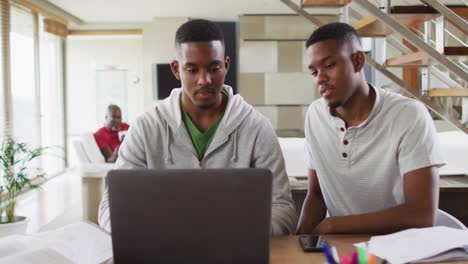 Two-african-american-teenage-twin-brothers-using-a-laptop-and-talking-with-father-in-background