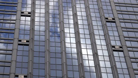 windows of a skyscraper reflect moving clouds in a blue sky