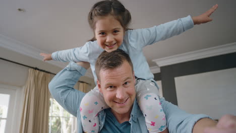 Padre-Feliz-Cargando-A-Una-Niña-Sobre-Sus-Hombros-Papá-Sosteniendo-A-Su-Hija-Disfrutando-De-Un-Juego-Lúdico-En-El-Concepto-De-Video-Chat-En-Casa-4k