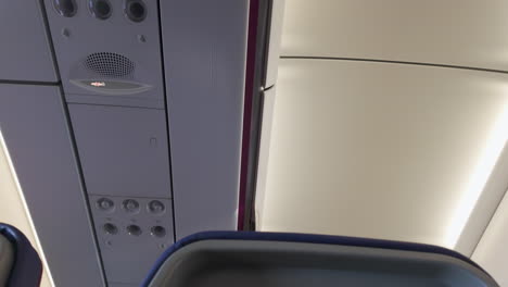 interior detail of an airplane, showing overhead panel with air vents, speakers, and cabin crew call button