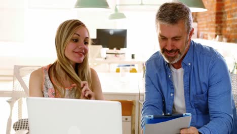 Male-and-female-executives-discussing-over-digital-tablet-at-desk