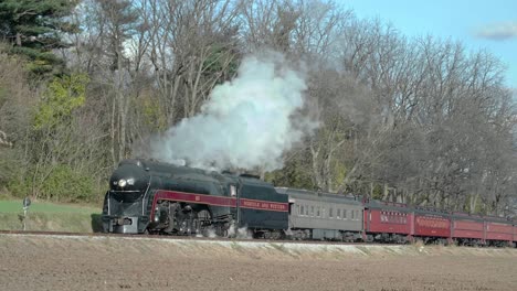 a vintage steam locomotive makes its way along the tracks, passing by leafless trees and a simple shelter. the autumn scenery presents a tranquil backdrop for this nostalgic journey.