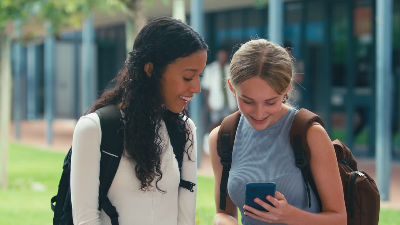Due studentesse di scuola superiore che guardano i social media sul telefono sedute all'aperto