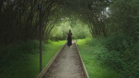 woman walking on a boardwalk through a lush green forest tunnel