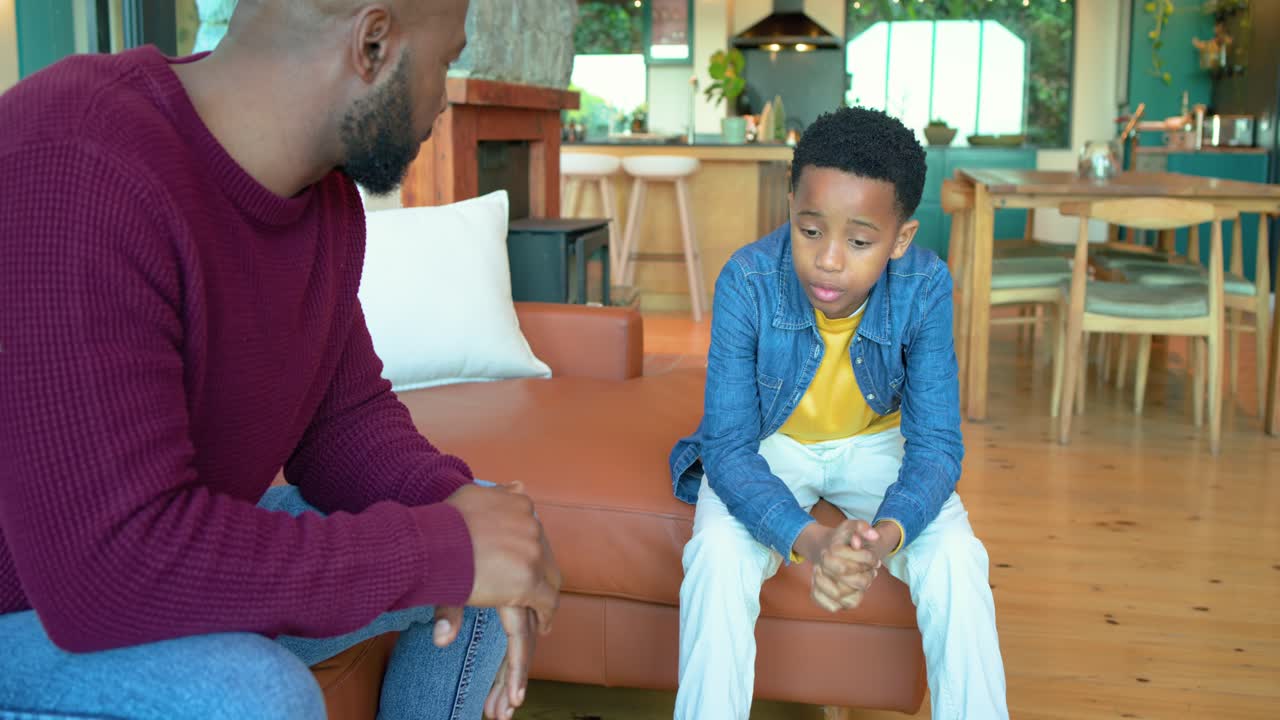 African American father clapping and encouraging anxious son fidgeting on sofa in living room