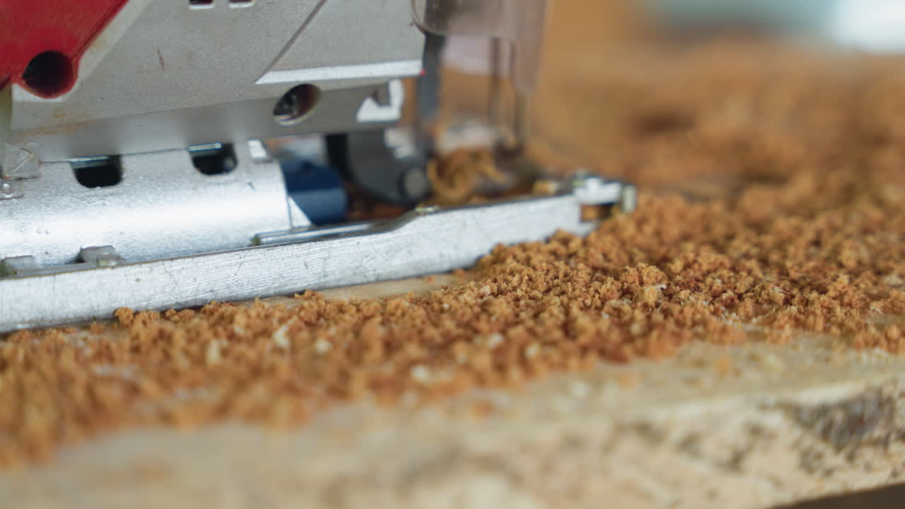 Nahaufnahme Stichsäge schneidet Spanplatte, Sägemehl fliegt, Werkbankdetail, kontrollierter, gleichmäßiger Schnitt, feine Späne häufen sich, Metallfuß und Sägeblatt sichtbar, handwerkliche Schreinertechnik, warmes Studiolicht