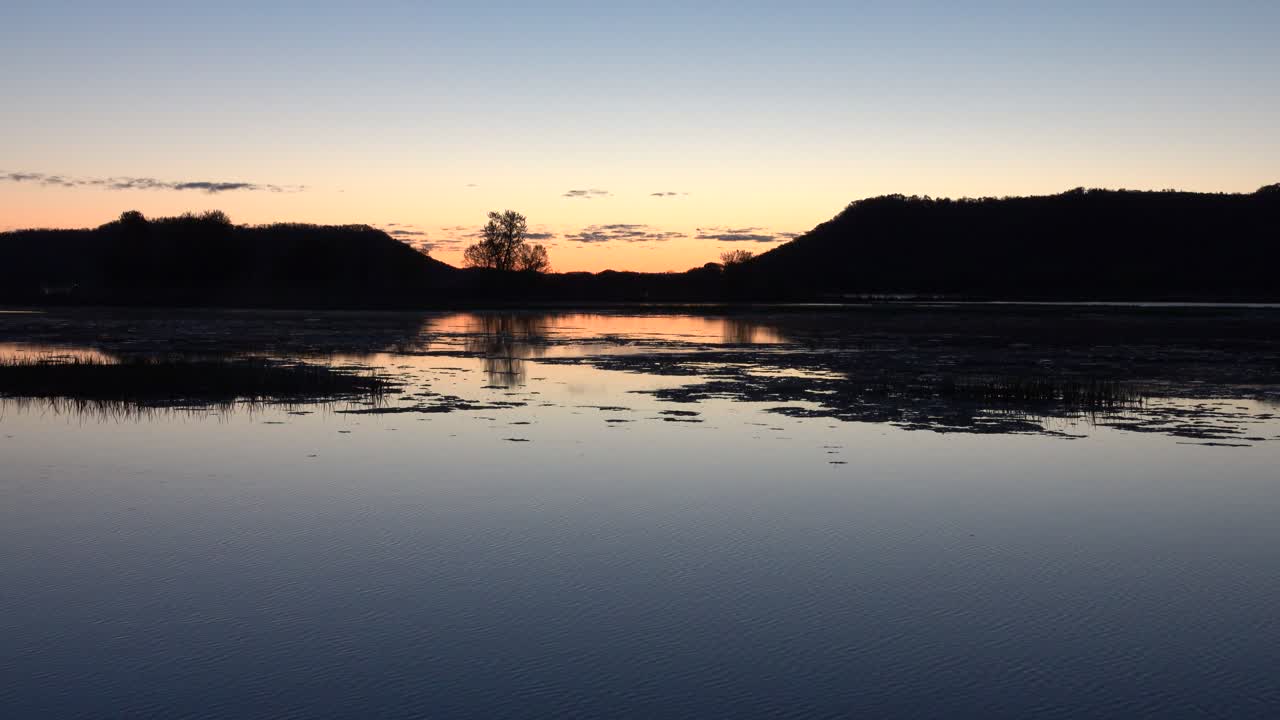 Riflesso di un tramonto sereno su un lago calmo con colline delineate