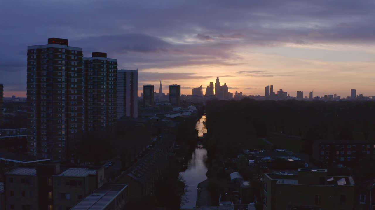 Niskie ujęcie z wózka do przodu. Lotnicze ujęcie z drona kanału Victoria Park w Londynie, w kierunku panoramy miasta o zachodzie słońca.