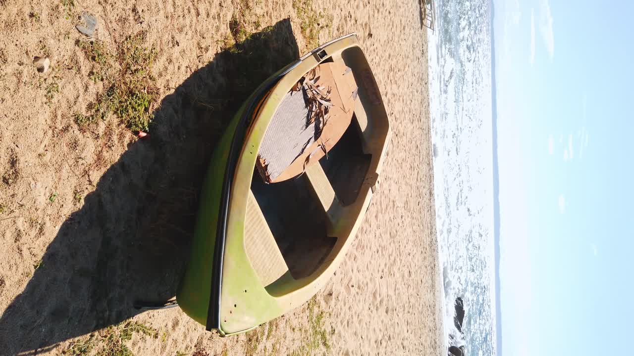 Beached boat made of green colored metal, waves of the Aegean sea on the background in Nikiti, Greece. Slow motion