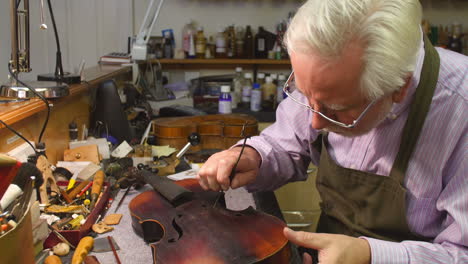 man restoring violin in workshop