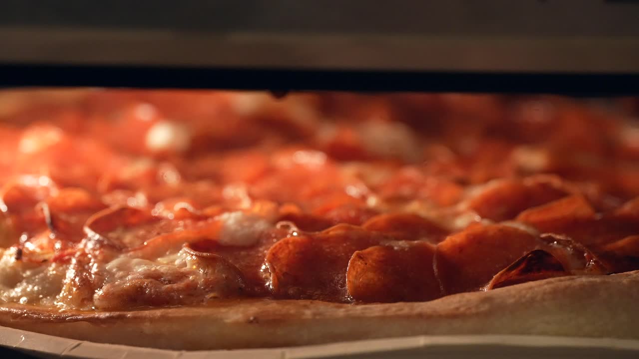 Pizza ai peperoni in cottura nel forno con il formaggio che si scioglie e bolle in primo piano.