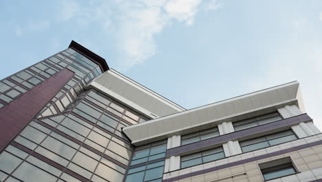 close rotational view of a modern city building with a sleek glass facade, highlighting its architectural details, with the perspective against a clear blue sky