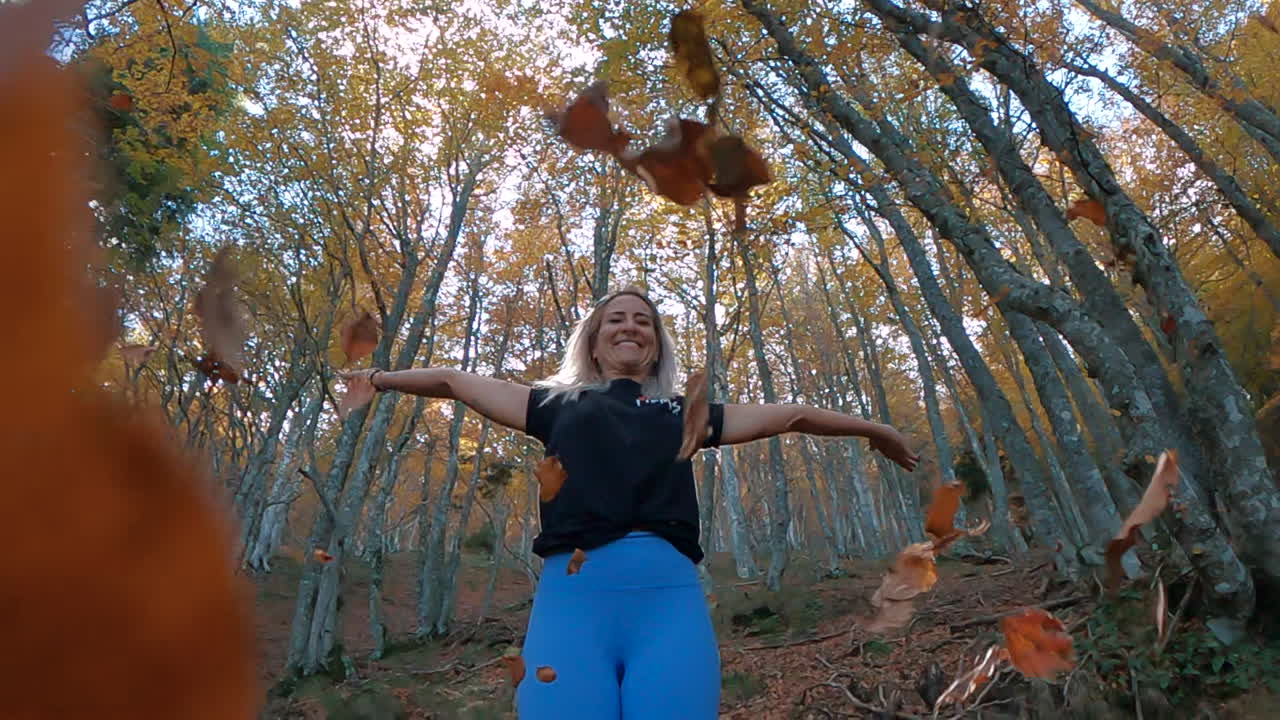 zoom en cámara superlenta de una mujer fitness que cae hojas de otoño en el bosque
