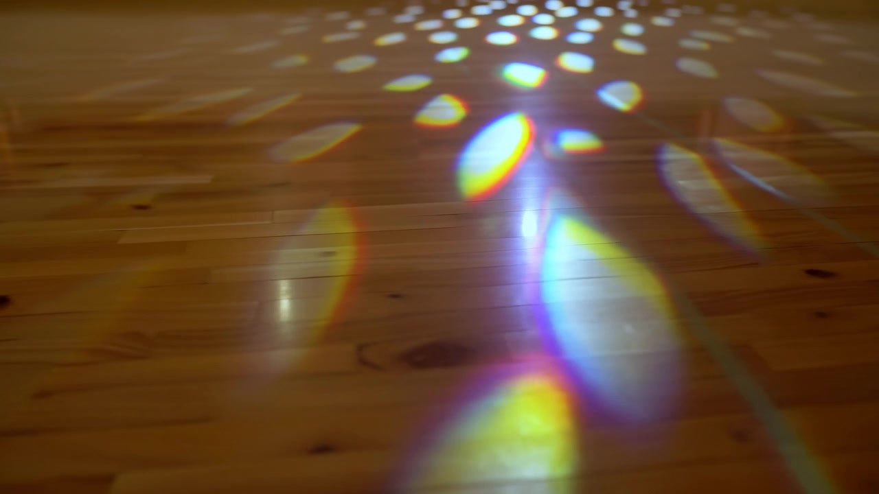 Vista diagonal próxima ao chão mostra tábuas de madeira brilhantes enquanto manchas de luz prismáticas ovais mudam de posição e brilho, criando reflexos de arco-íris, destaques suaves e textura decorativa sutil.