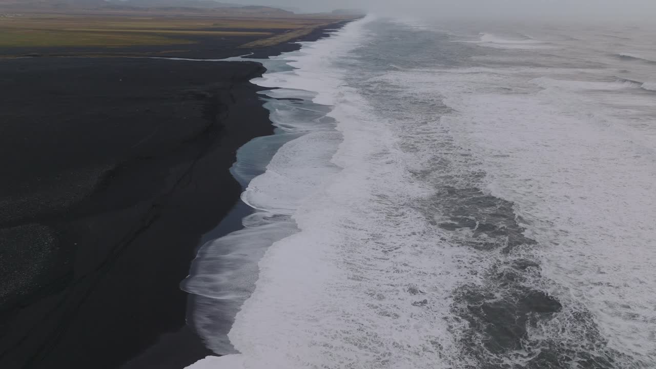 Aerial landscape view of ocean waves crashing on Iceland S&oacute;lheimasandur black sand beach, on a moody day