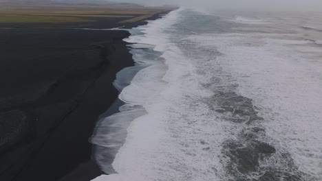 Aerial-landscape-view-of-ocean-waves-crashing-on-Iceland-Sólheimasandur-black-sand-beach,-on-a-moody-day
