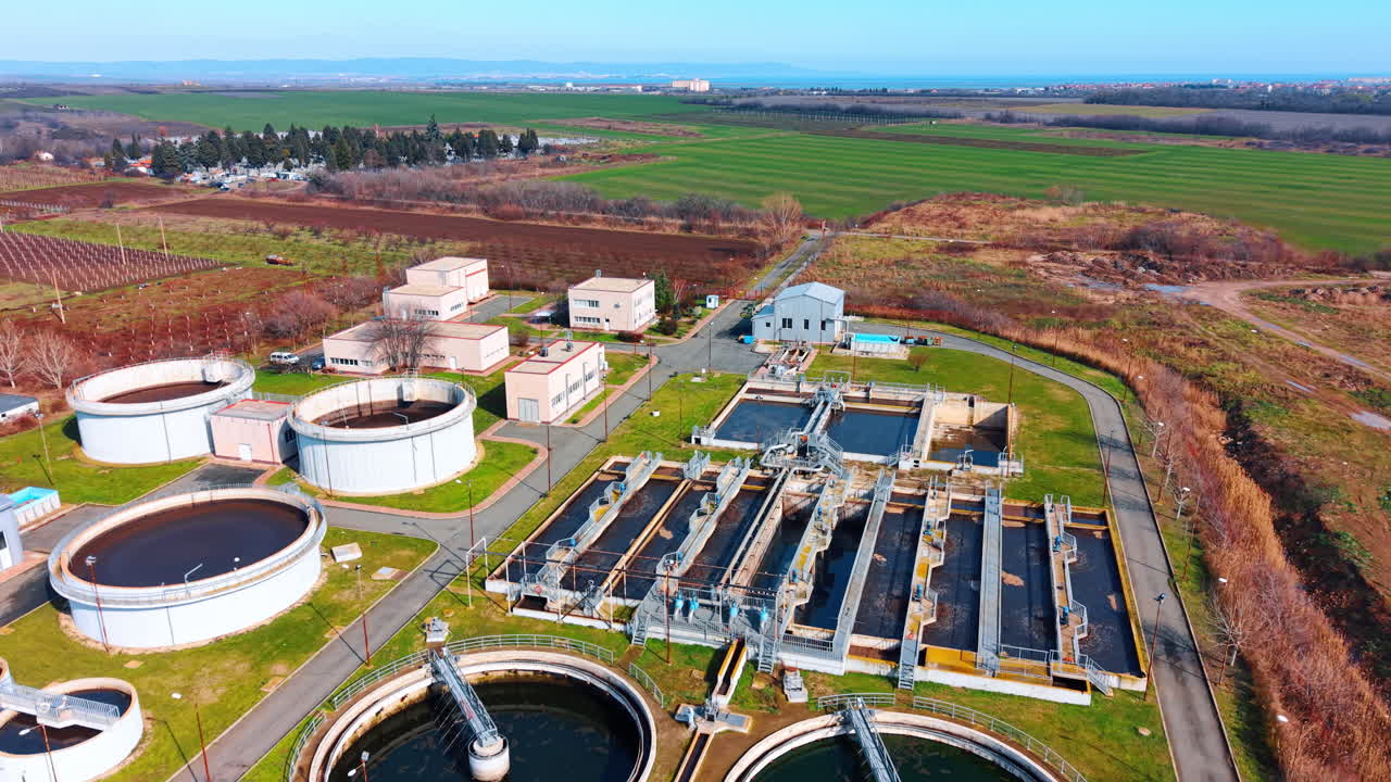 Aerial view of municipal wastewater treatment plant facility. Drone shot of industrial sewage treatment plant with circular clarifiers and rectangular aeration tanks in rural area
