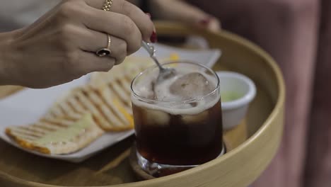 young woman slowly whisk with metal spoon to an iced tea in a glass cup