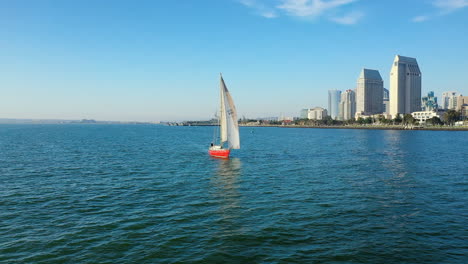 red sailboat on the san diego bay with a view of san diego's skyline