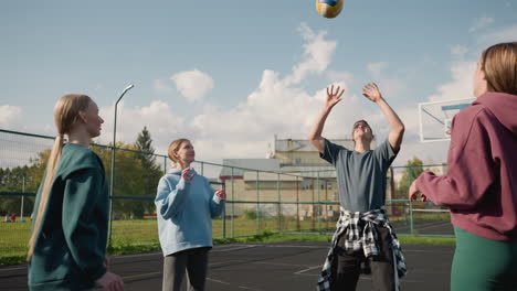 training session with three ladies playing volleyball amongst themselves, coach with plaid shirt around waist, in outdoor court with basketball hoop and fence in background