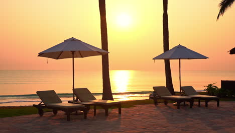 Sun-umbrella-and-deckchair-empty-on-sandy-beach-with-sea-in-background-at-sunset