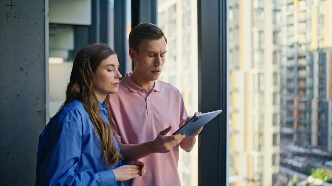 Closeup company managers talking tasks near window. Architects analyzing tablet