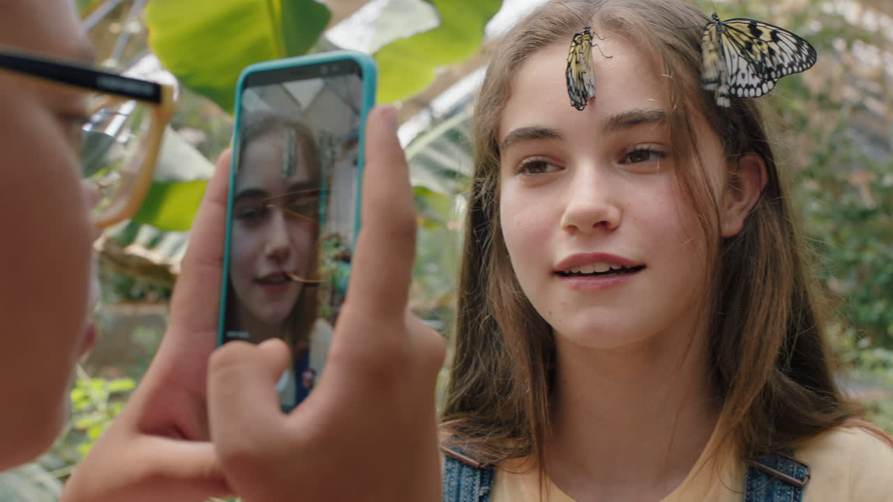 hermosas mariposas en la cara de las niñas con un amigo feliz tomando fotos usando un teléfono inteligente amigos divirtiéndose en el zoológico santuario de vida silvestre compartiendo una excursión en las redes sociales imágenes 4k