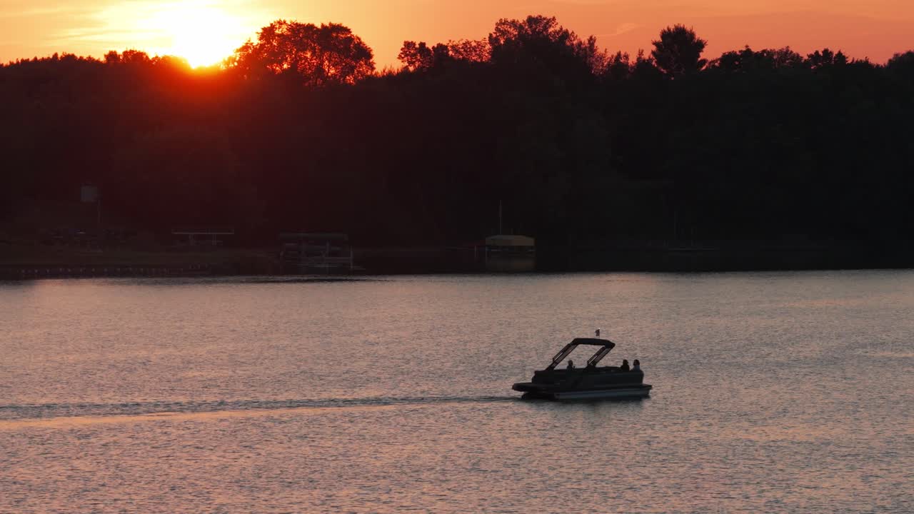 Telephoto dolly aerial shot of a pontoon boat at sunset on North Center Lake in Minnesota. 4K
