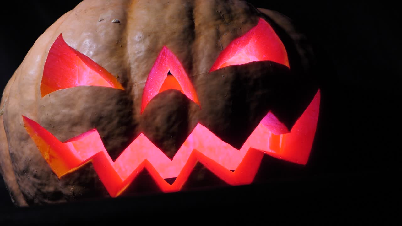 calabaza de halloween con una cara aterradora y una araña en el ojo, iluminada desde el interior con luces multicolores, una calabaza muy aterradora para halloween