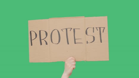 hand holding cardboard with protest sign, green chromakey background. hand showing protest cardboard banner. chroma key screen background.