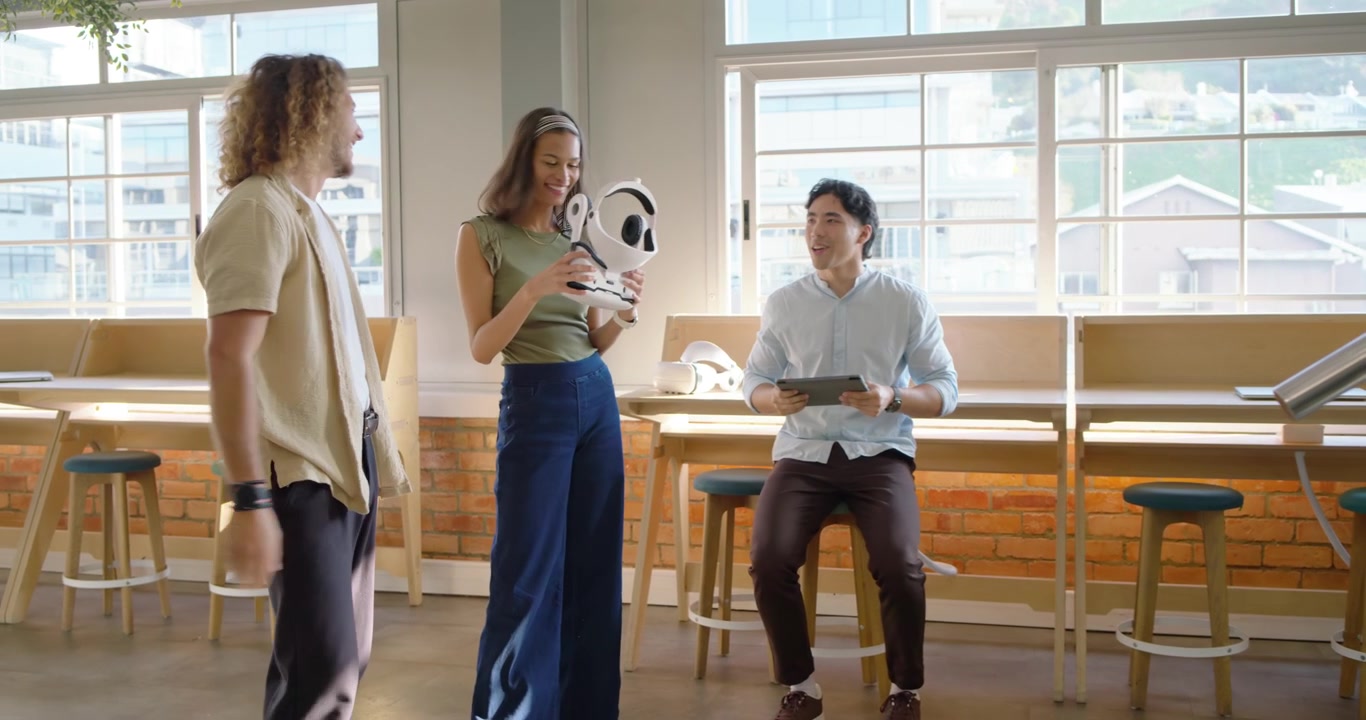 Đội ngũ đa dạng trong phòng chờ đang xem người phụ nữ đeo tai nghe VR màu trắng, người đàn ông làm cô ấy giật mình, để lộ một con robot