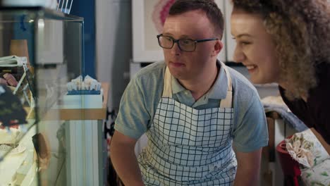 caucasian waiter with down syndrome advising client a dessert from the fridge in a cafe.