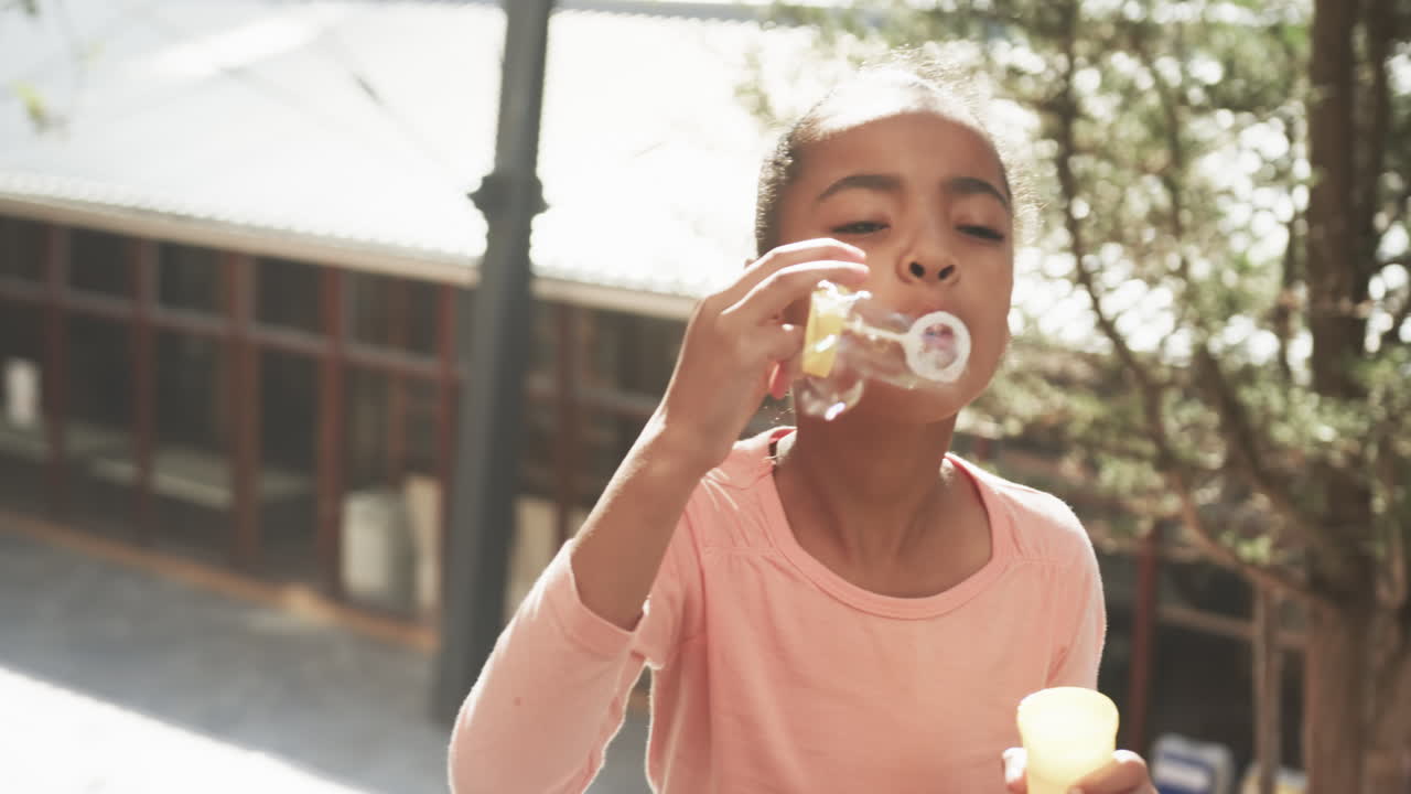Blowing bubbles, African American girl enjoying outdoor activity at school, having fun
