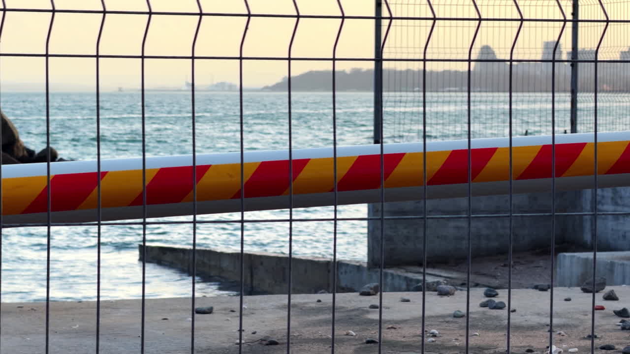Barrera en el paseo marítimo cerca del agua durante las horas de la tarde. Una valla con una barrera roja y amarilla bloquea el acceso a la zona del paseo marítimo al atardecer.