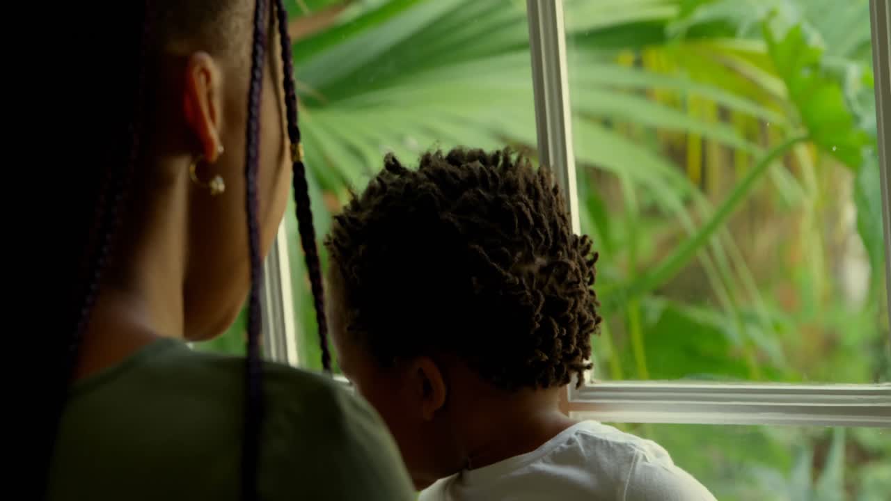 Rear view of young black mother playing with his son on window sill in a comfortable home 4k