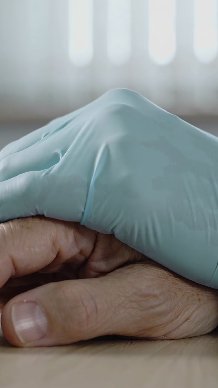 Close-up of Gloved Hand Comforting Elderly Hand