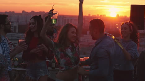 grupo de amigos disfrutando de una fiesta en una terraza al atardecer, todos bailan y ríen 1