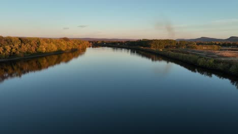 connecticut river, hadley massachusetts, fall colors at sunset, aerial dolly over calm peaceful rivers with soft glow of light in sky on horizon