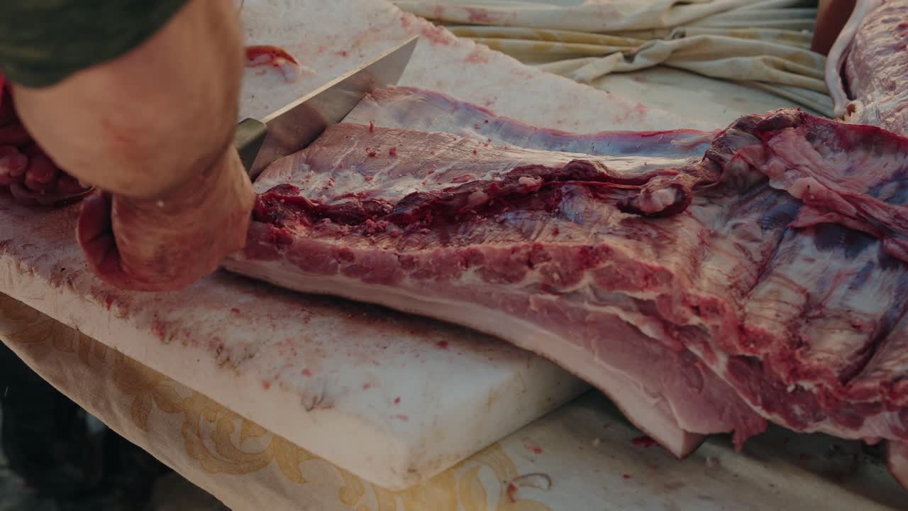 close up of pork ribs being cut by hand on an outdoor table