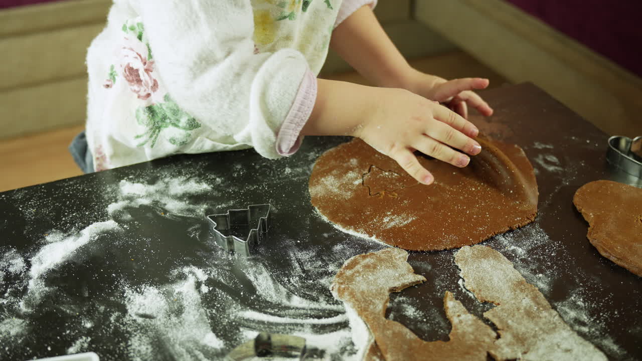 Child small hands pressing star and heart gingerbread shapes into flour-dusted dough on a board during Christmas cookie preparation in a warm festive kitchen filled with holiday tradition