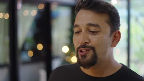 a man with a beard smiling and talking indoors